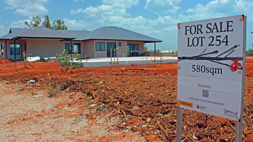 A for sale sign outside a house surrounded by red earth.