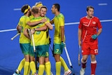 A group of Australian men's hockey players hug after a goal, as a dejected England player stands by.