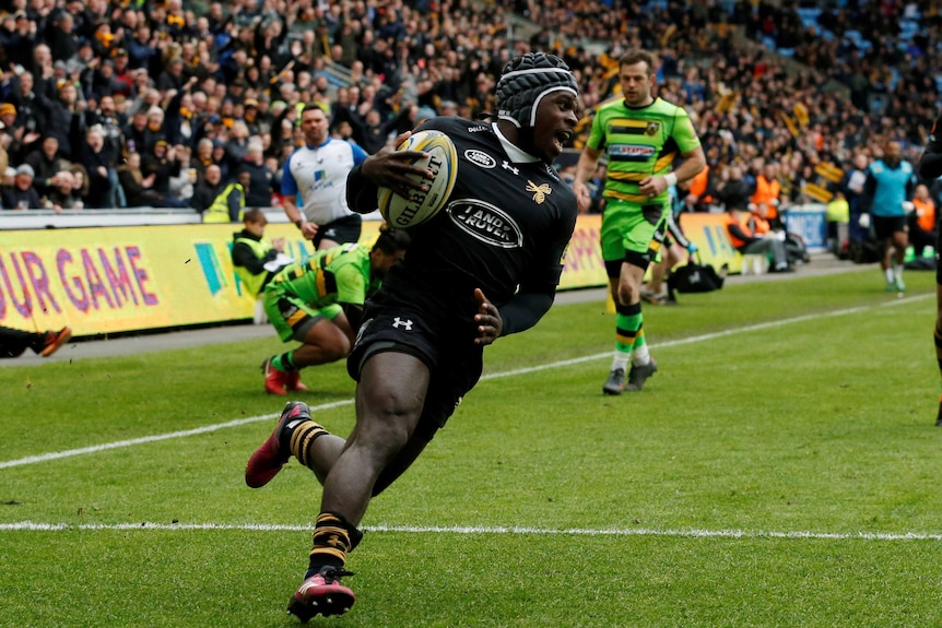 A rugby union player tucks the ball under his arm as he runs in to score a try.