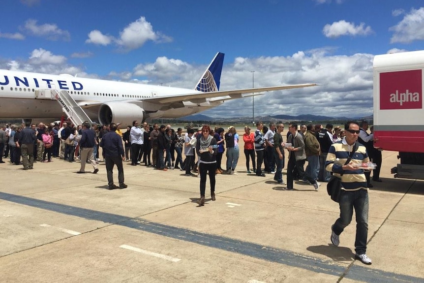 Stranded United Airlines passengers line up for food on the tarmac in Canberra.