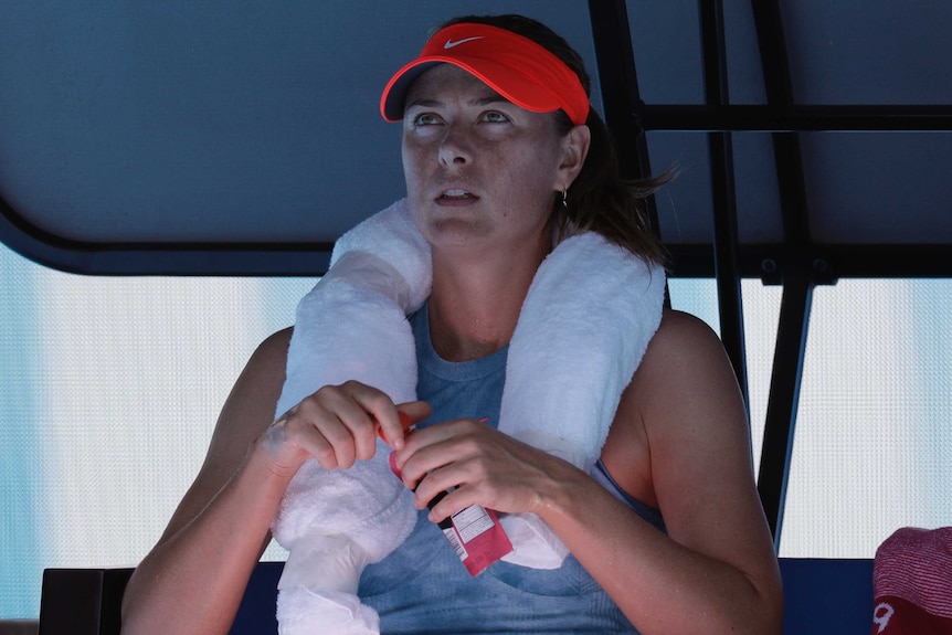 Woman sitting down at the change of ends in a tennis match with a wet towel around her neck.