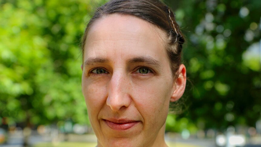 Woman with brown hair with green tree canopy behind.