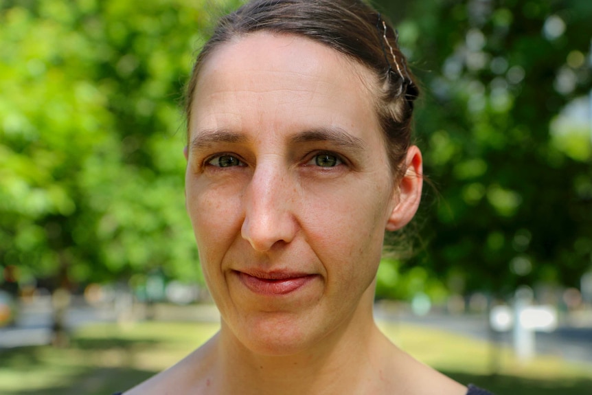 Woman with brown hair with green tree canopy behind.