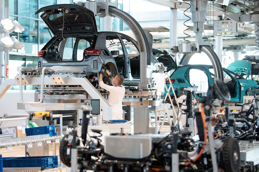 A man drills together a partially assembled car in a busy factory