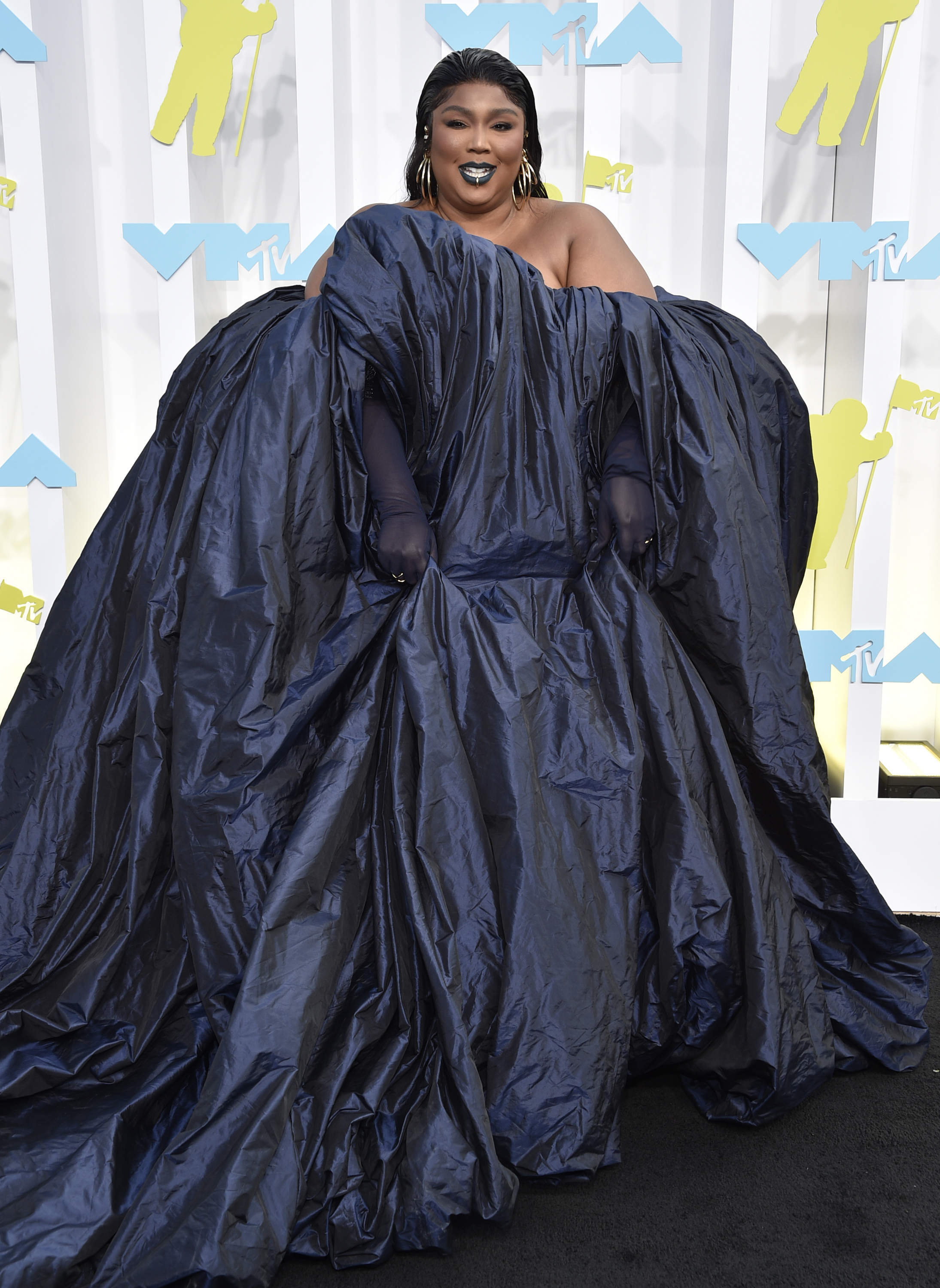 lizzo smiles on mtv vmas red carpet wearing a full-length layered navy blue gown, long gloves and gold jewellery