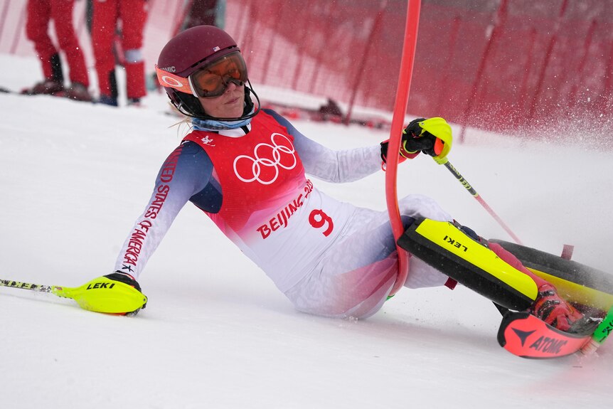 A skier looks away as she slides on the snow into a gate to fail to finish her run in a slalom event.  