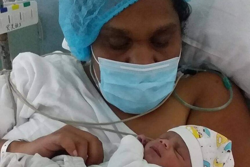 Mother in face mask holds her new baby in hospital. 
