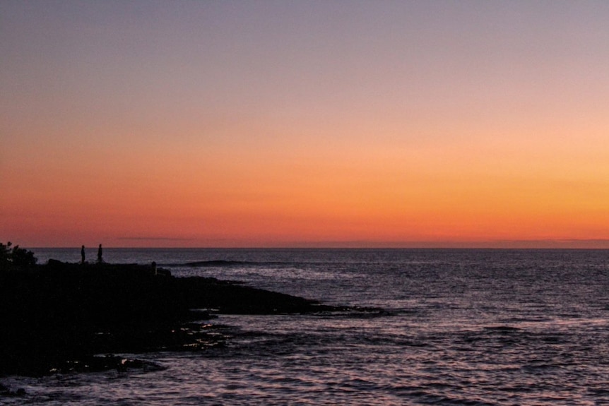 Two people watch the orange sunset over the beach on Tanna in Vanuatu.