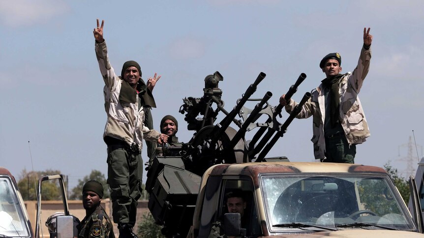 Four Libyan National Army (LNA) members wearing army clothes gesture peace signs from a car mounted with guns.