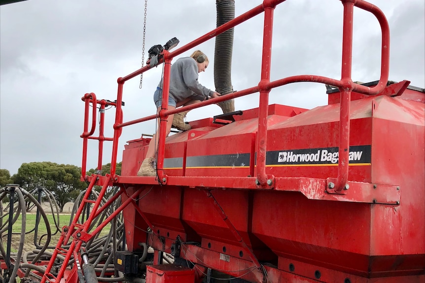 A large, red item of farm machinery, with a person on top of it