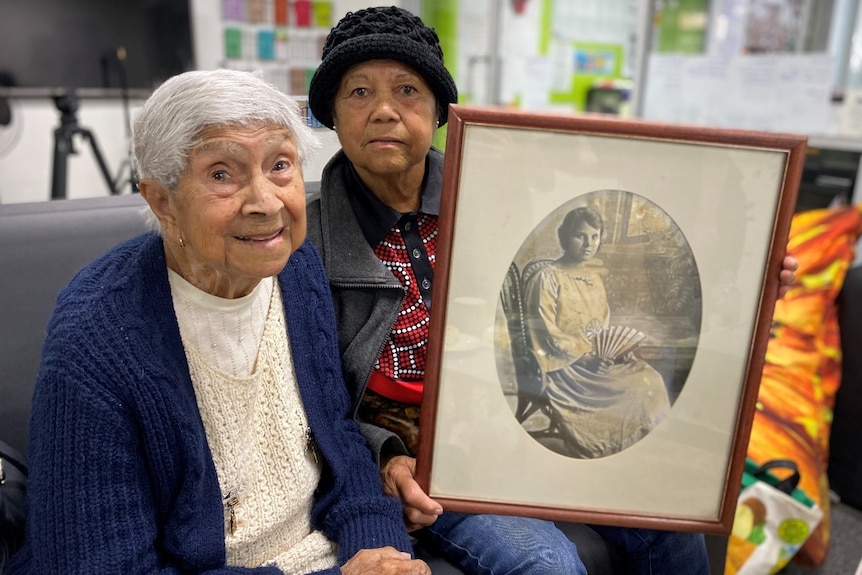 two women sitting down, one is holding a frame with a picture of a woman sitting down