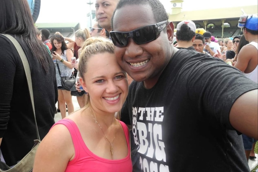 Tara and Luke Kaspar smile together at the camera. They look like they are at a music festival, with people behind them.