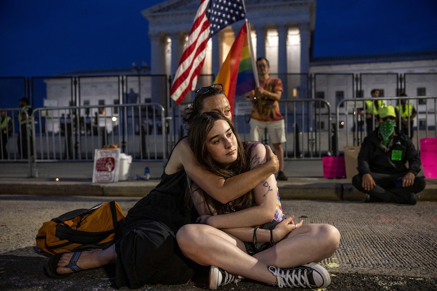 Outside the US Supreme Court, a woman sits cross legged with her arms wrapped around a teenaged girl
