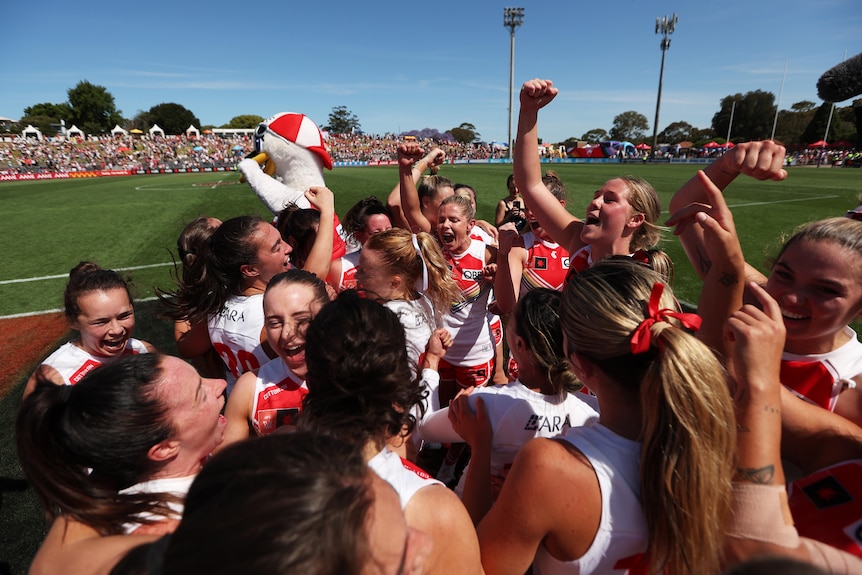 A group of AFLW players celebrate a win over Collingwood