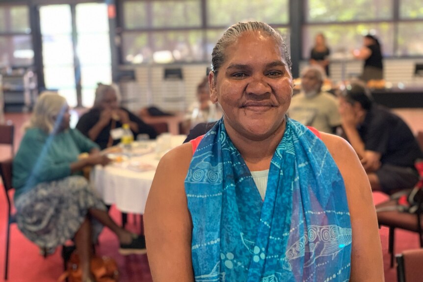 Portrait shot of a middle-aged Aboriginal woman wearing a blue scarf, she's looking into the camera and smiling.
