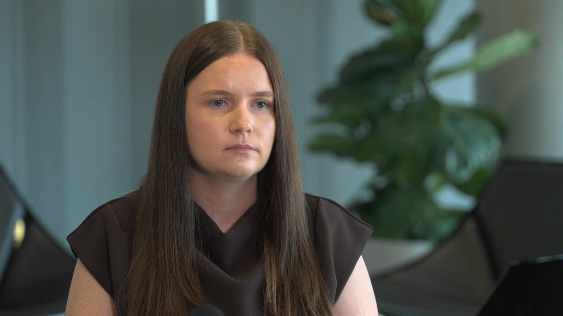Mulher com cabelo castanho e top preto, olhando para longe da câmera