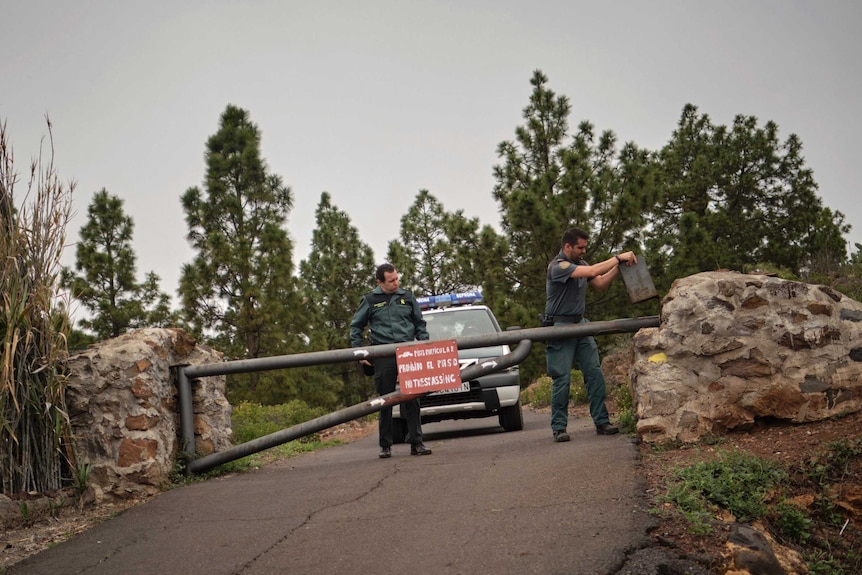 Two police officers close a boom gate on a road with a patrol car parked behind them