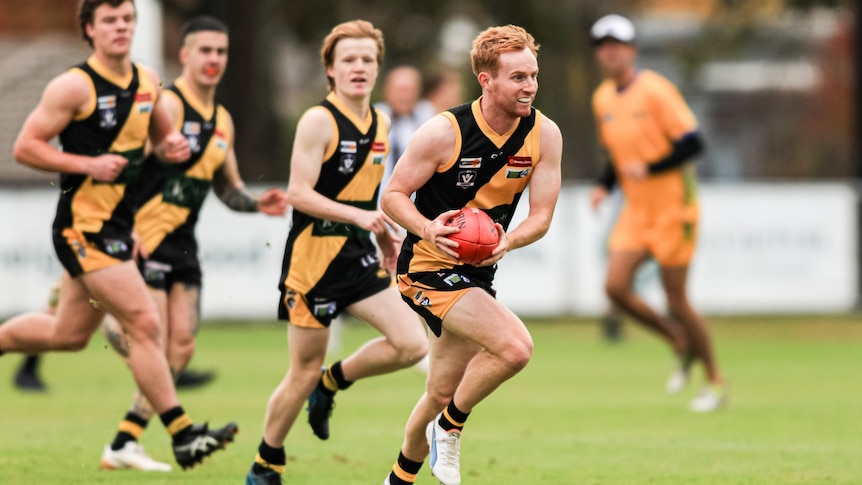 A man runs while holding a football and is pursued by his teammates.