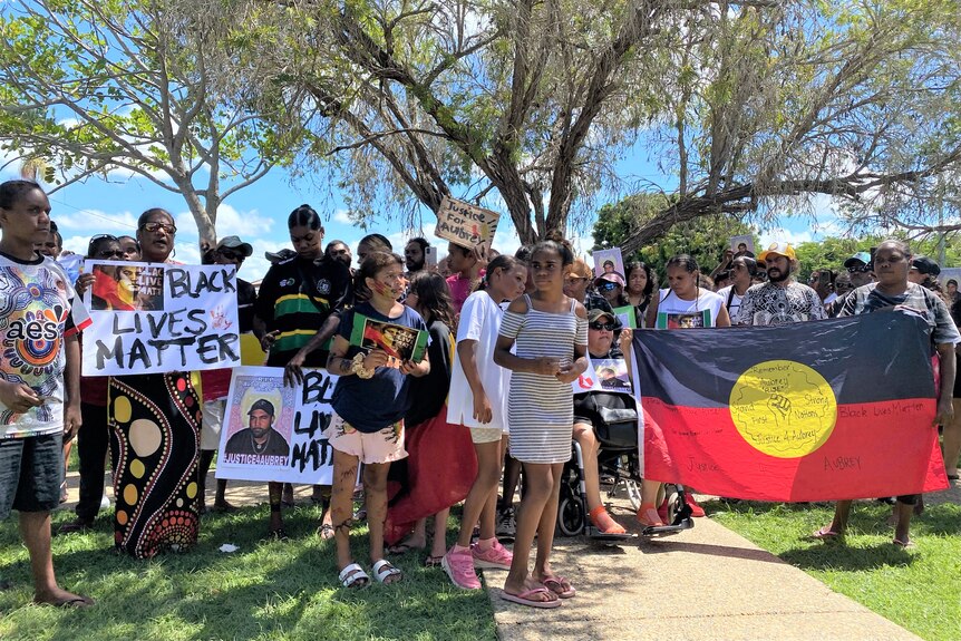 A large group of protesters gather, displaying Black Lives matter signs and the Aboriginal flag