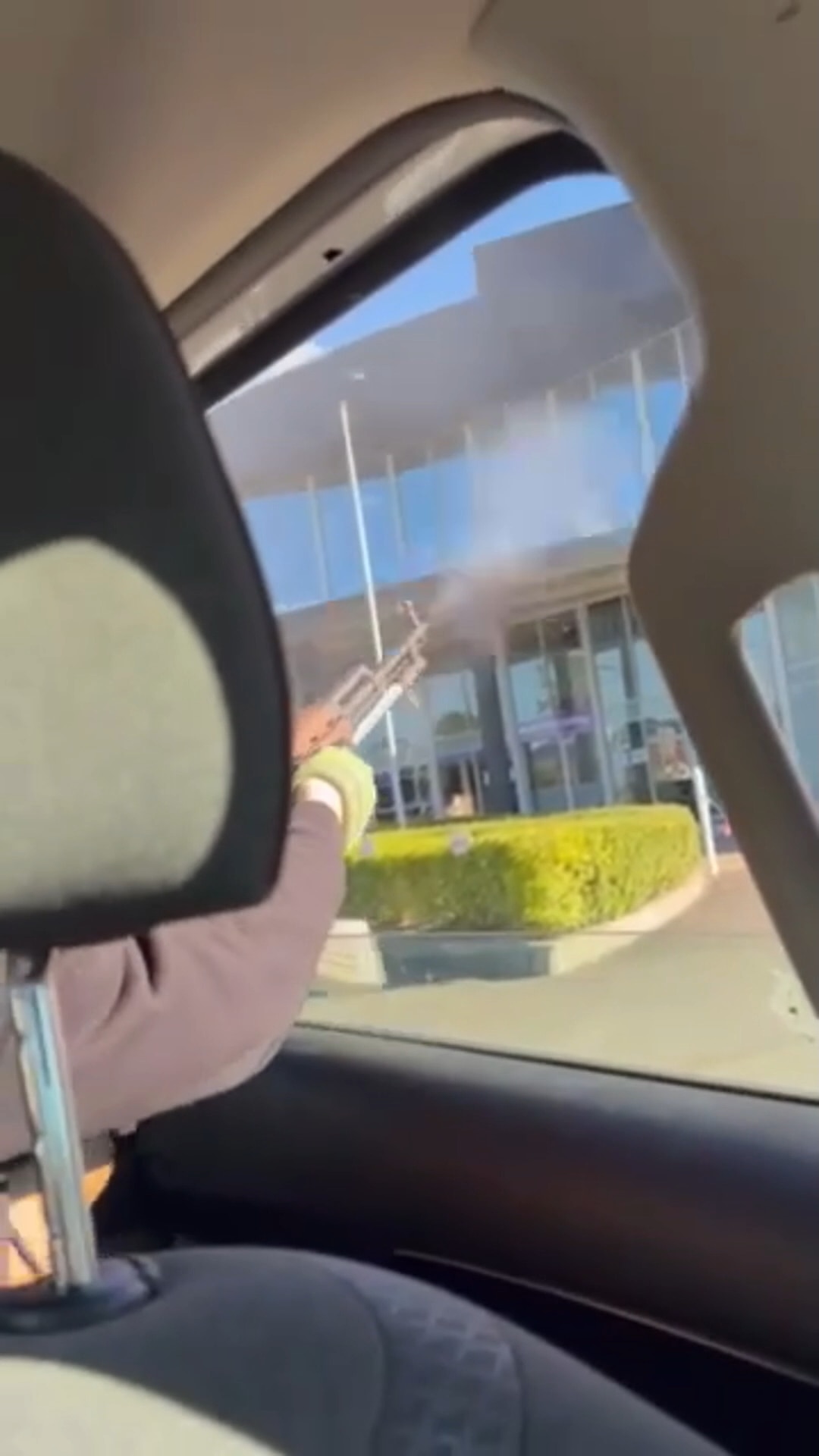 Semi-automatic rifle barrel outside an car window with smoke coming out end. Glass and dark building in background