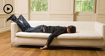 Man lays face down on a white couch with arm hanging down and feet in the air.