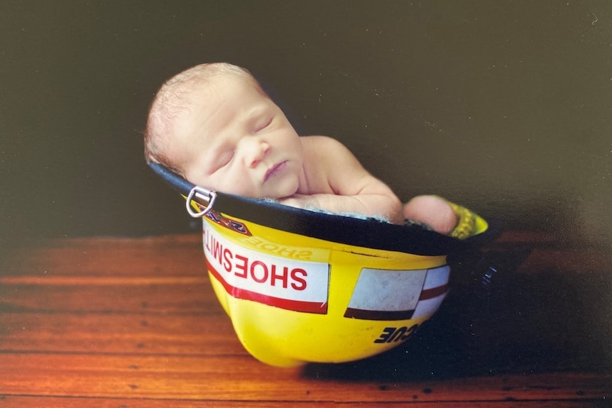 A young baby sleeps inside a yellow firefighter's helmet.