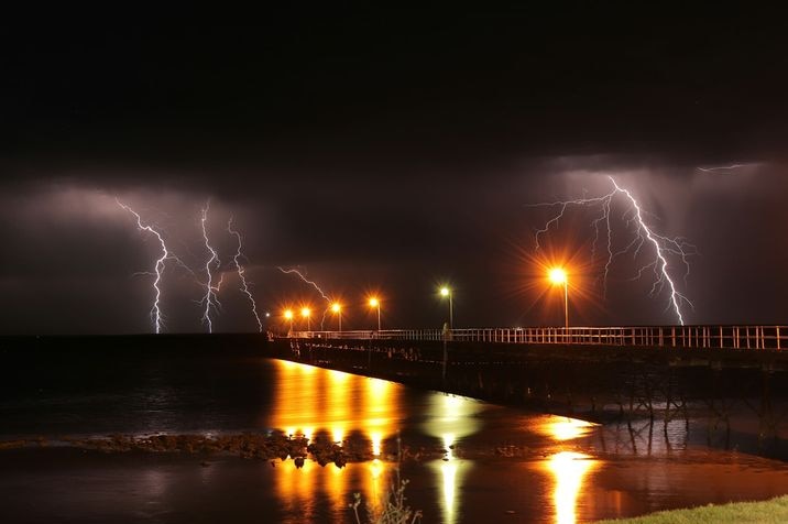 Four lightening bolts behind a jetty at night.
