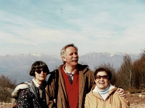 Two women and a man stand in front of a mountain range.