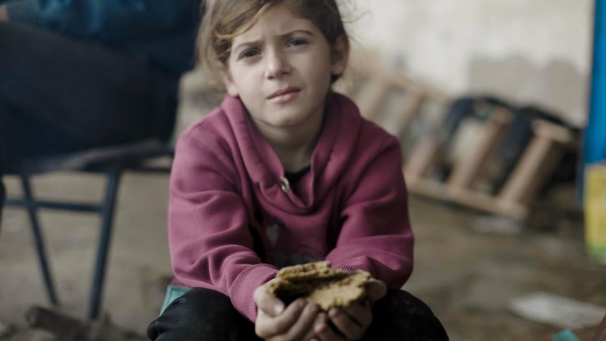 A young girl wearing a pink jumper holds a piece of bread made from animal feed.