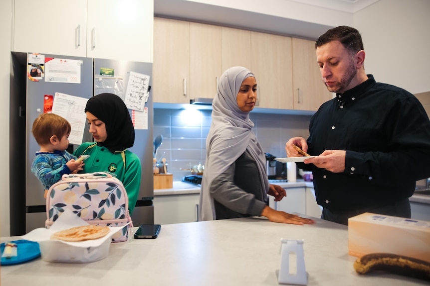 Ramy and Athirah stand in the kitchen with their family, getting ready for the day.