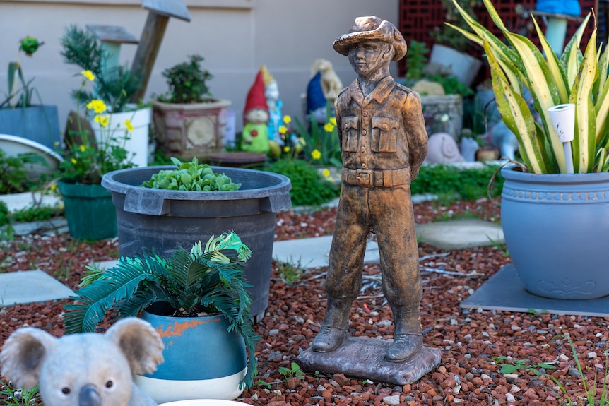 A statue of a brown soldier among pot plants, gravel and gnomes