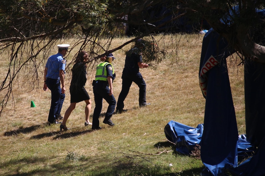 Police and other officials walk near a tree.