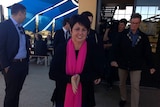 Alyssa Hayden, wearing a pink scarf, and standing in the foreground, with a cameraman and Liberal party officials behind her.