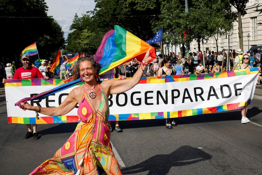 A woman waves a rainbow flag at the front of a parade