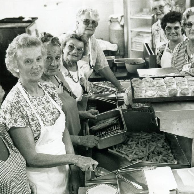 Black and white of a group of older women cooking chips and scones