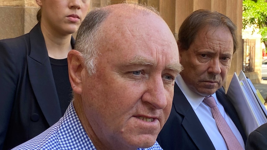 A bald man outside a sandstone building