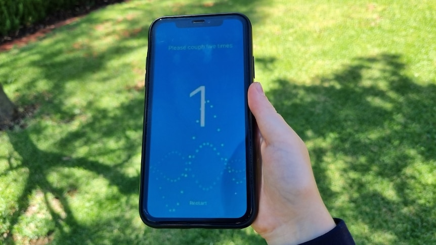 A smartphone being held in a child's hand with a blue cough screening application open, green lawn in background