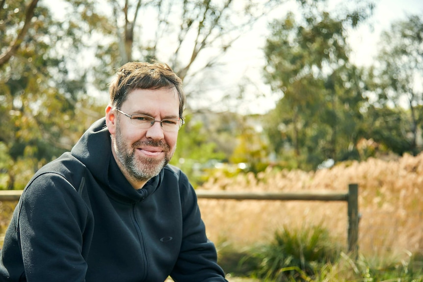 Cameron Solnordal sitting in a field, he is smiling and wearing glasses.