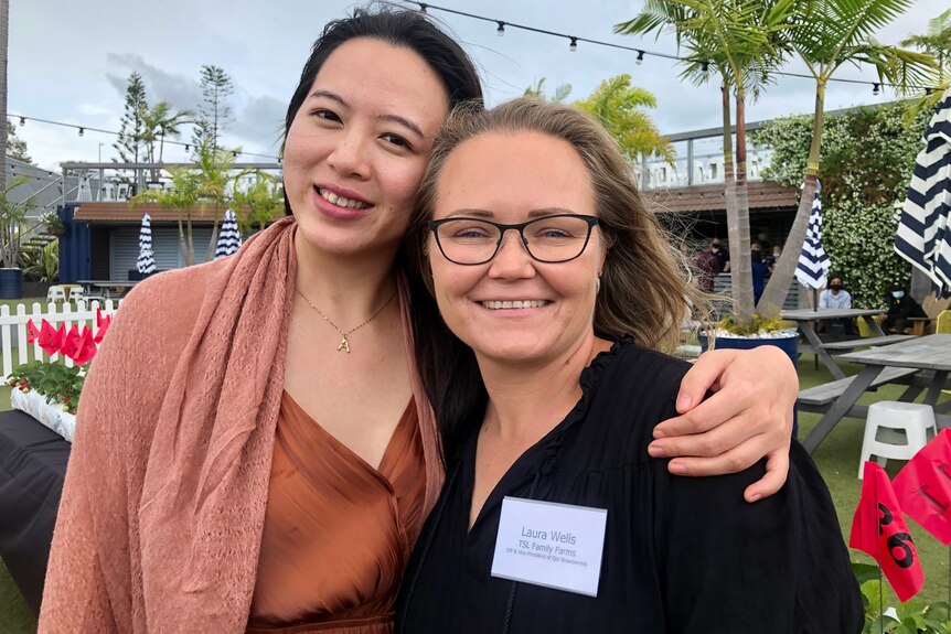 Two ladies hug and smile at the camera.