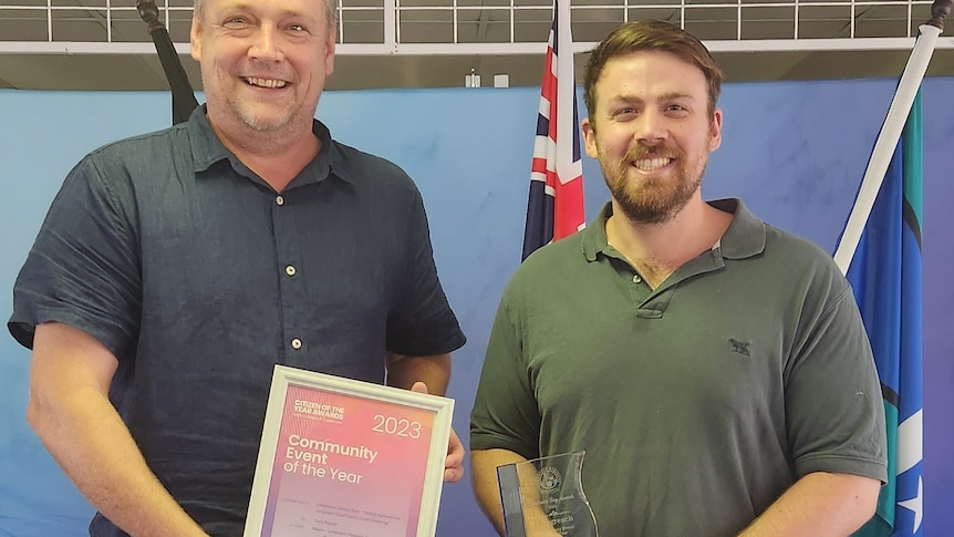 Two men stand with a certificate. Man on the right has blonde hari, man on left has brown hair