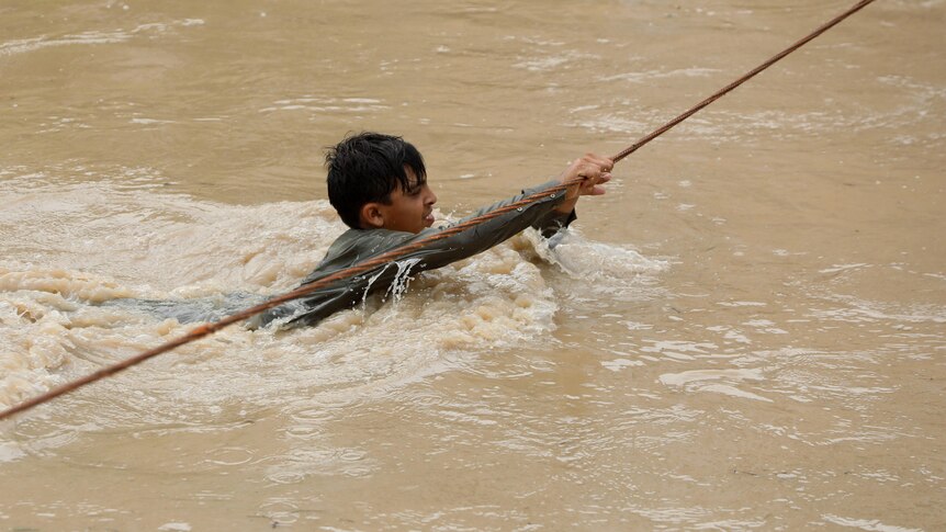 Boy tries to cross flooded street with rope.