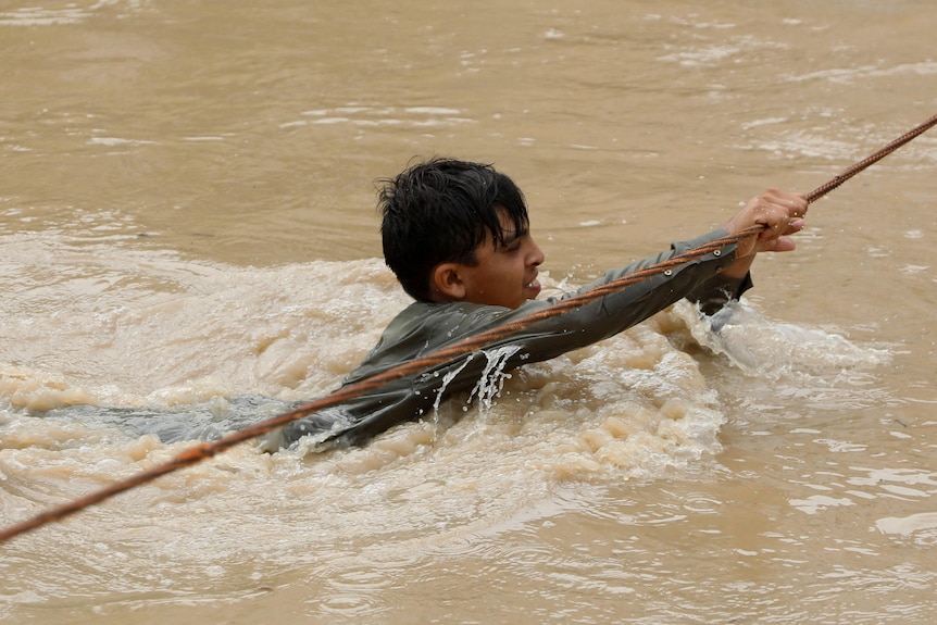 Boy tries to cross flooded street with rope.