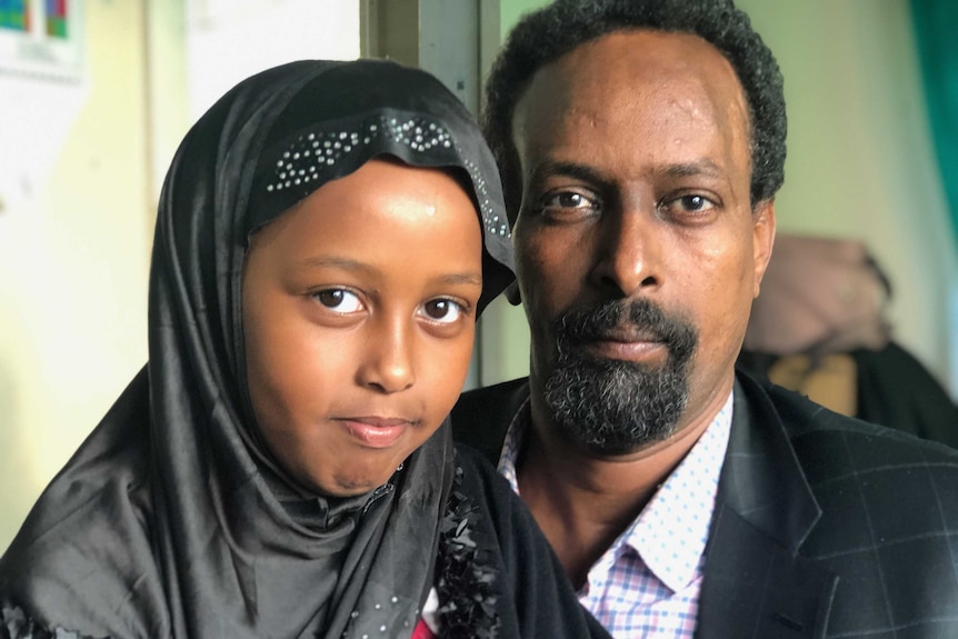 A man wearing a suit jacket smiles with a young girl wearing a headscarf.