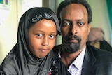 A man wearing a suit jacket smiles with a young girl wearing a headscarf.