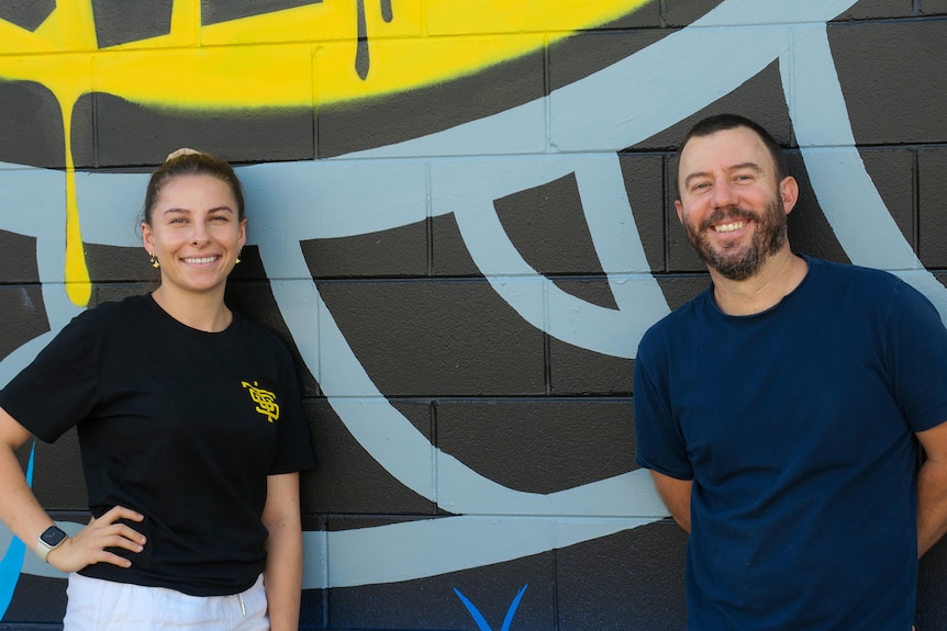 Matt Noffs stands in front of a mural at the Street University with engagement officer Grace Rogers.