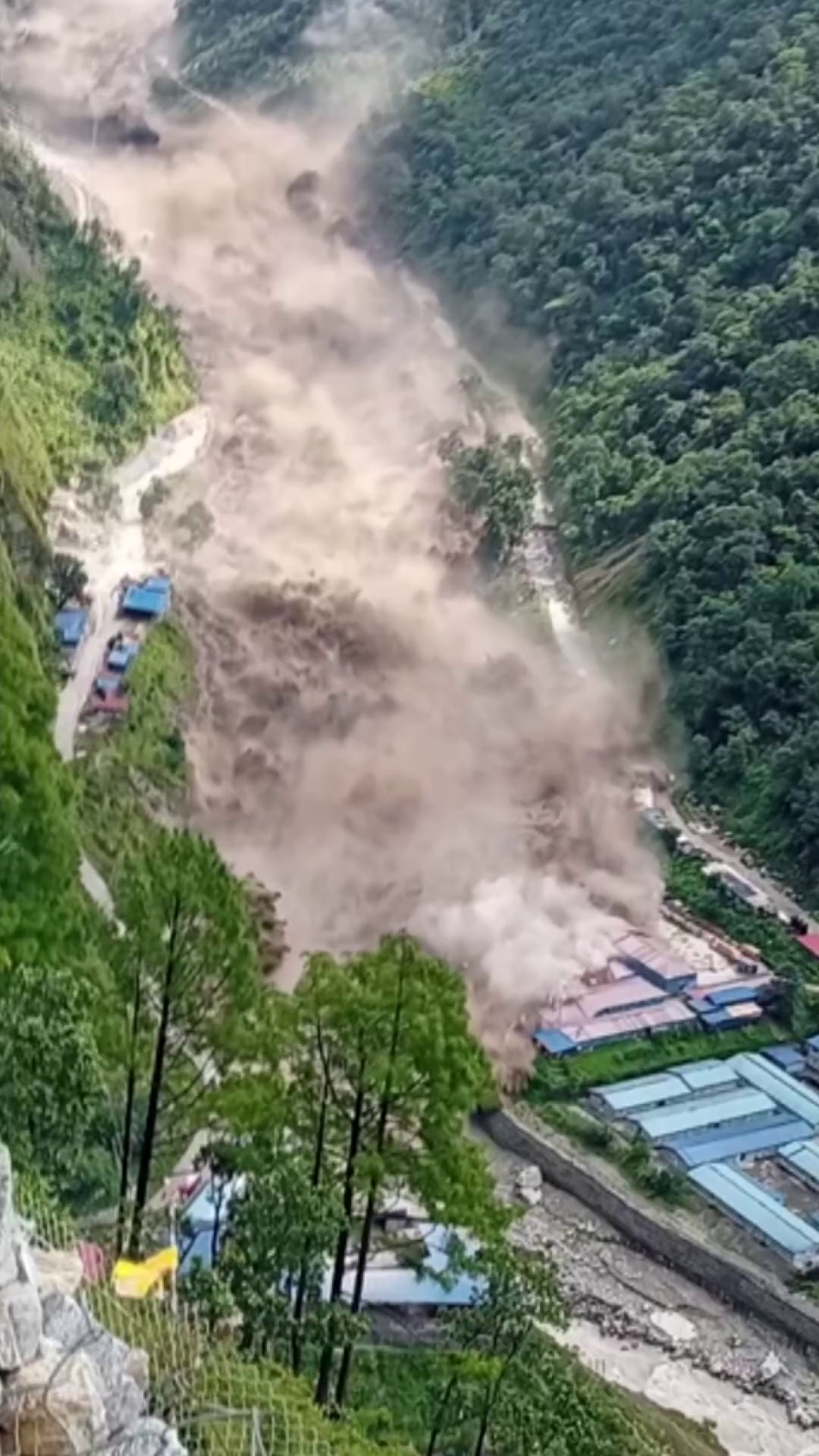 Torrent of murky water engulfs an engineering basecamp situated in a valley.
