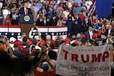 President Donald Trump stands at a podium to speak in front of a crowd at a campaign rally