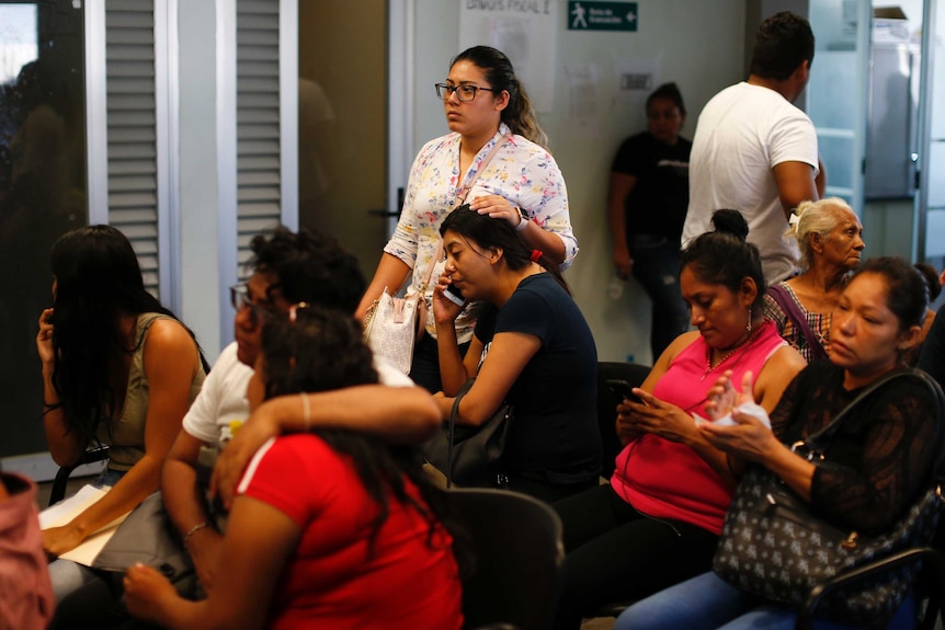 Female relatives of the victims, some weeping and embracing, sit in a government office waiting to identify loved ones.