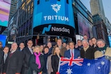 A crowd holding an Australian flag with a large Tritium/Nasdaq advert in the background
