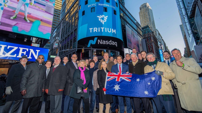 A crowd holding an Australian flag with a large Tritium/Nasdaq advert in the background